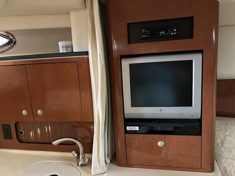 Slide: The Image of 2005 Sea Ray 320 Sun Dancer interior with TV, sink, and wooden cabinetry. - 8