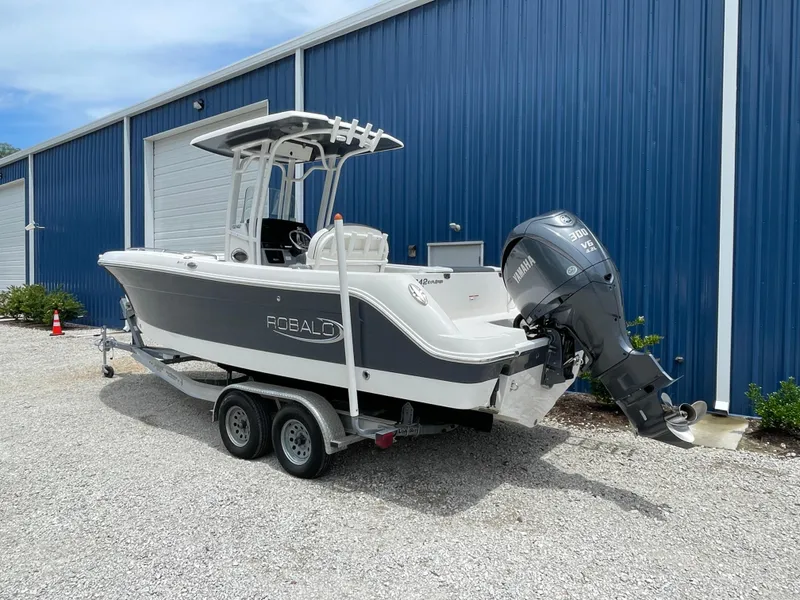 Slide: The Image of 2021 Robalo R242 Explorer boat on trailer, parked near blue building. - 2