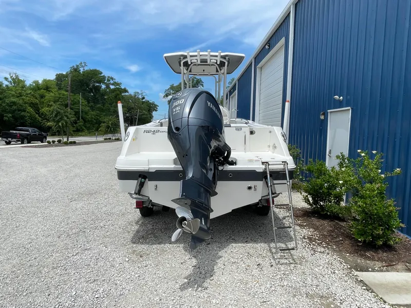 Slide: The Image of 2021 Robalo R242 Explorer boat with outboard motor, parked near a blue building. - 3