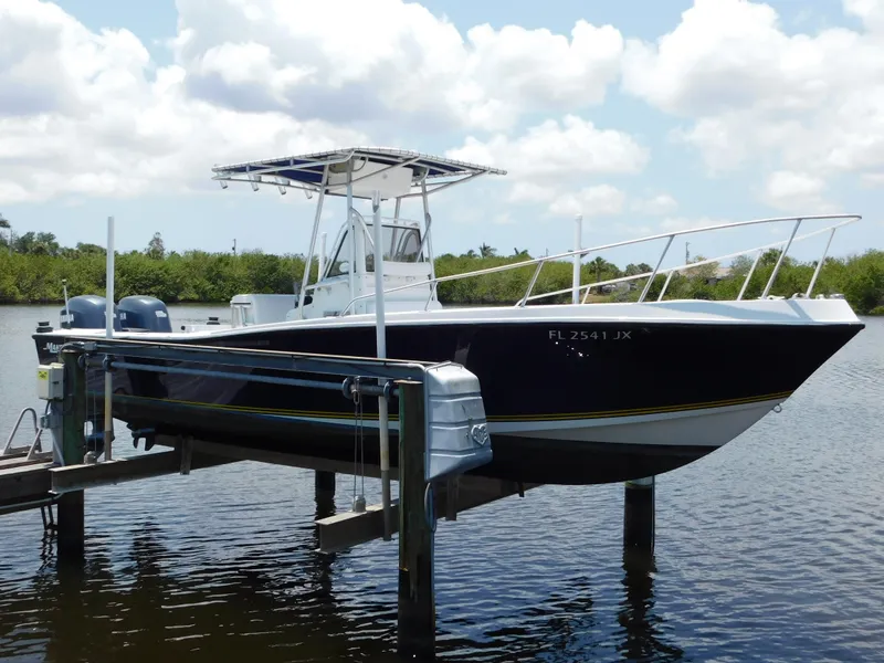 Slide: The Image of 1985 Mako 254 Center Console boat on lift, with dual engines, under a partly cloudy sky. - 1