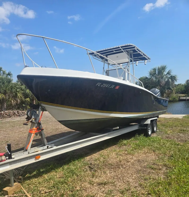 Slide: The Image of 1985 Mako 254 Center Console boat on trailer, parked near water under blue sky. - 6