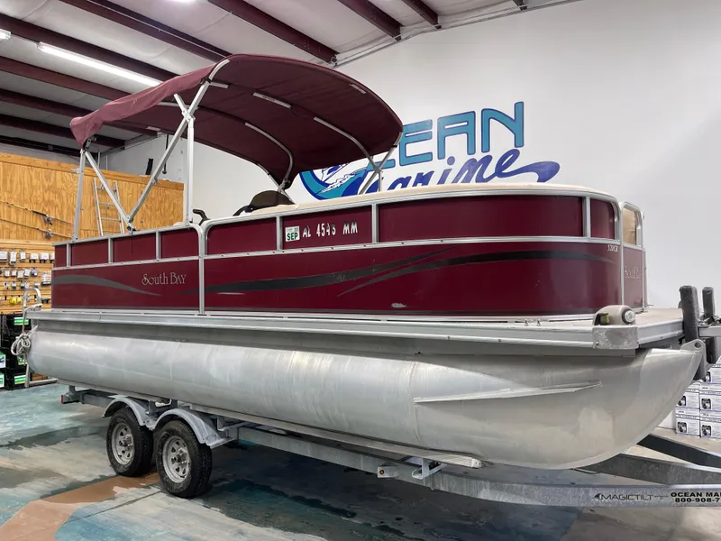 Slide: The Image of 2010 South Bay 520CR pontoon boat with maroon canopy on trailer in showroom. - 3