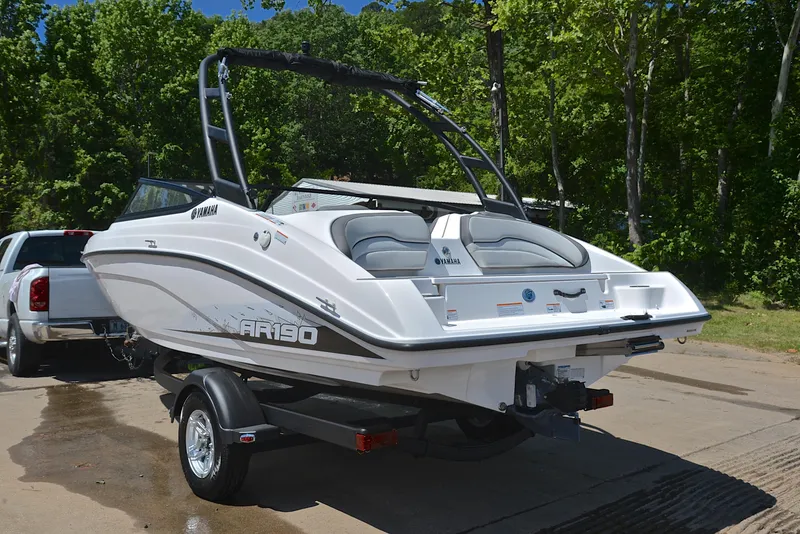 Slide: The Image of 2023 Yamaha AR190 boat on trailer, parked outdoors with lush green trees in the background. - 12