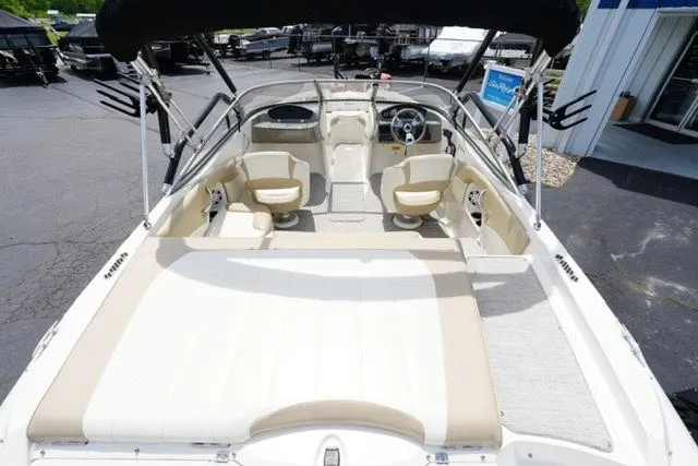 Slide: The Image of 2016 Stingray 208LR boat interior with beige seating and steering wheel, parked outdoors. - 6