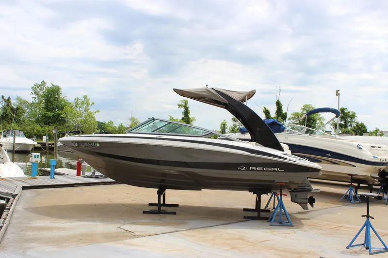 The Image of 2012 Regal 2100 RS Bowrider on stands at a marina, cloudy sky background. - 1