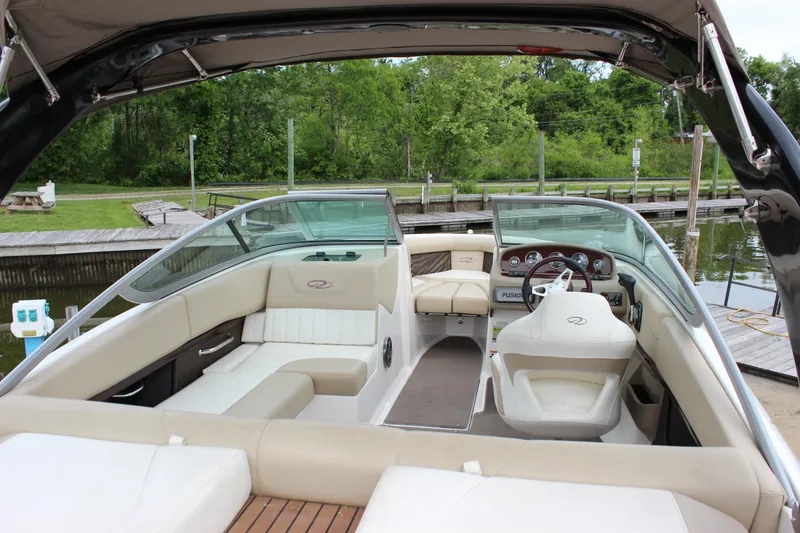 Slide: The Image of 2012 Regal 2100 RS Bowrider interior with beige seating and dashboard, docked by lush greenery. - 9