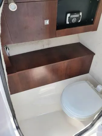 Slide: The Image of 2016 Robalo R227 Dual Console boat interior with compact marine toilet and wooden cabinetry. - 27