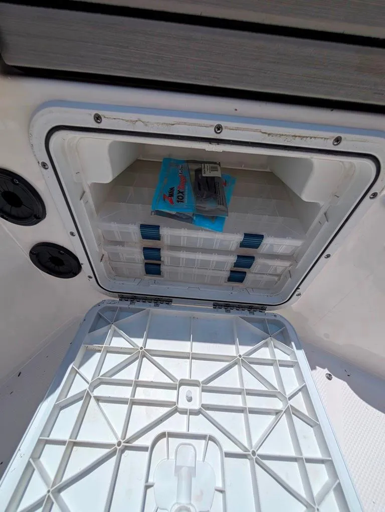 Slide: The Image of Open storage compartment on 2021 Yamaha Boats 195 FSH Sport, showing organized tackle boxes. - 24
