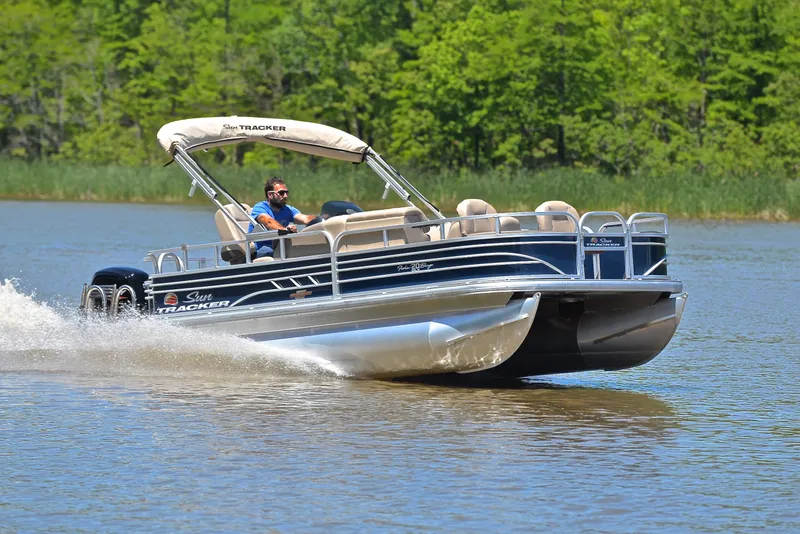 The Image of 2023 Sun Tracker Fishin Barge 20 DLX cruising on a lake with lush green background. - 1