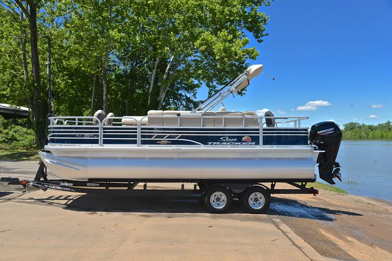 Slide: The Image of 2023 Sun Tracker Fishin Barge 20 DLX pontoon boat on trailer by a lake. - 11