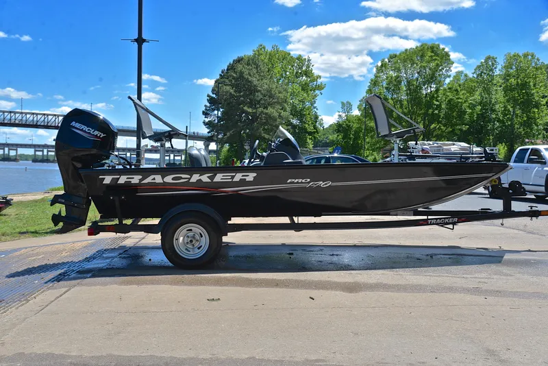 Slide: The Image of 2023 Bass Tracker Pro 170 boat on trailer by a river, under a clear blue sky. - 15
