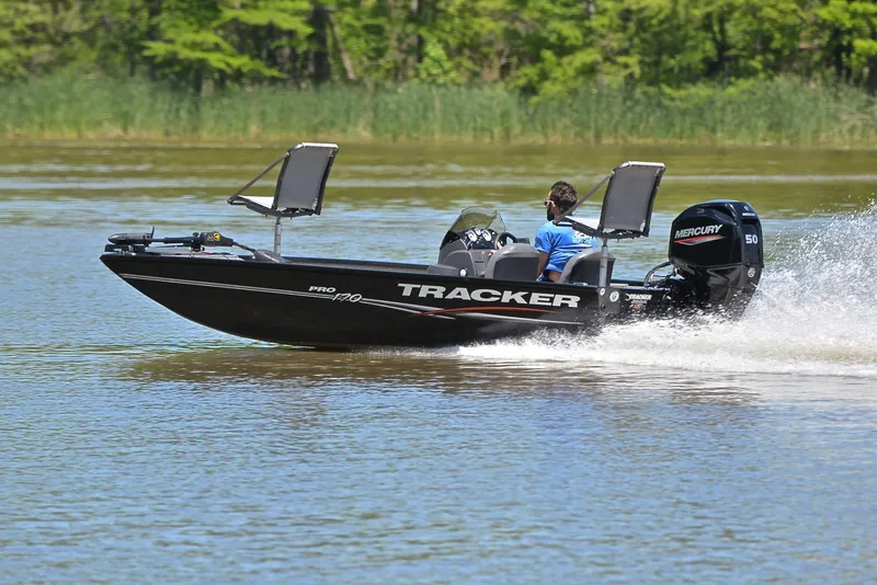 Slide: The Image of 2023 Bass Tracker Pro 170 boat speeding on a lake with lush greenery. - 4