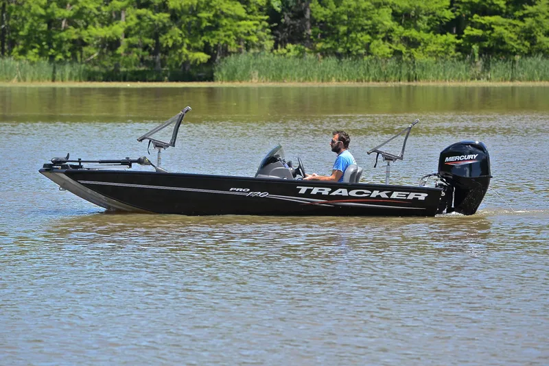 Slide: The Image of 2023 Bass Tracker Pro 170 boat on a calm lake with lush greenery. - 9