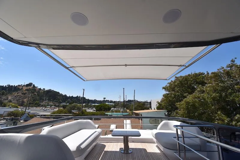 Slide: The Image of 2024 Azimut Fly 68 yacht flybridge with seating, table, and sunshade, overlooking marina and trees. - 26