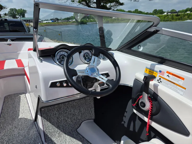 Slide: The Image of 2014 Glastron GT 185 boat interior with steering wheel and dashboard, near a scenic lake. - 13
