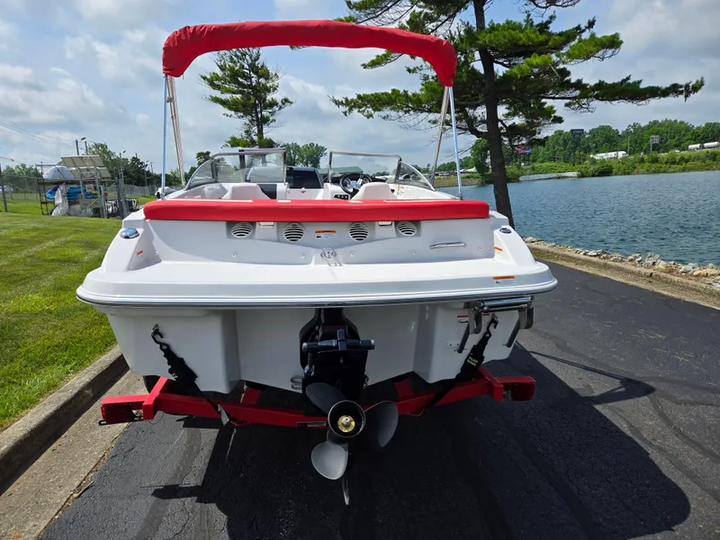 Slide: The Image of 2014 Glastron GT 185 boat with red canopy, parked near a lake. - 2