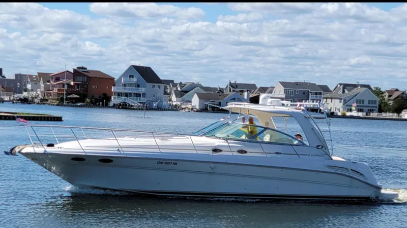 Slide: The Image of 2003 Sea Ray 410 Express Cruiser on water near coastal homes under blue sky. - 0