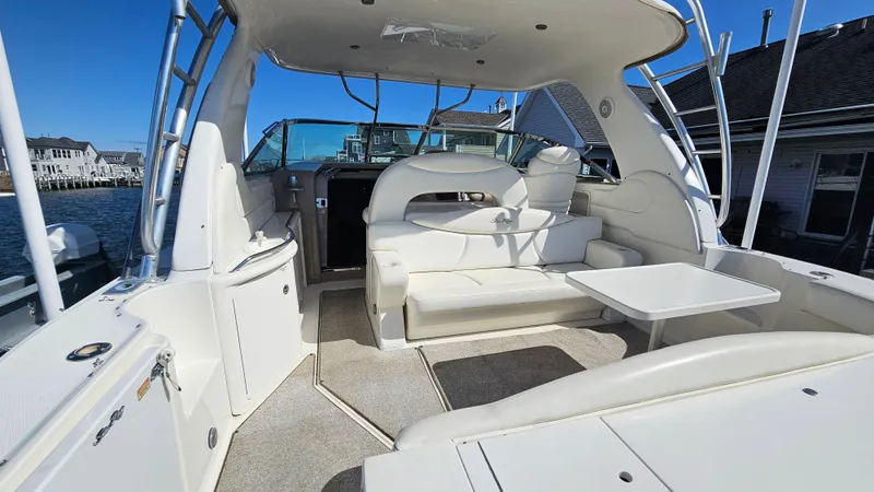 Slide: The Image of 2003 Sea Ray 410 Express Cruiser interior with white seating and table, docked by waterfront homes. - 13
