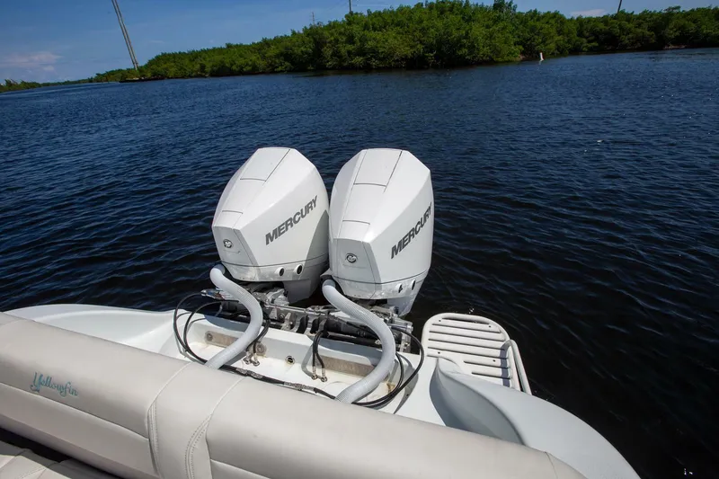 Slide: The Image of Twin Mercury outboard engines on a 2022 Yellowfin 26 Hybrid boat, near lush shoreline. - 13