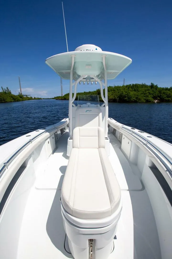 Slide: The Image of 2022 Yellowfin 26 Hybrid boat on calm water, clear sky, lush greenery. - 16
