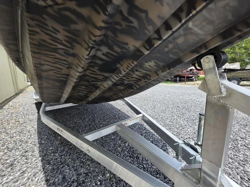 Slide: The Image of 2025 Xpress XP180 boat on trailer, camo design, parked on gravel. - 2