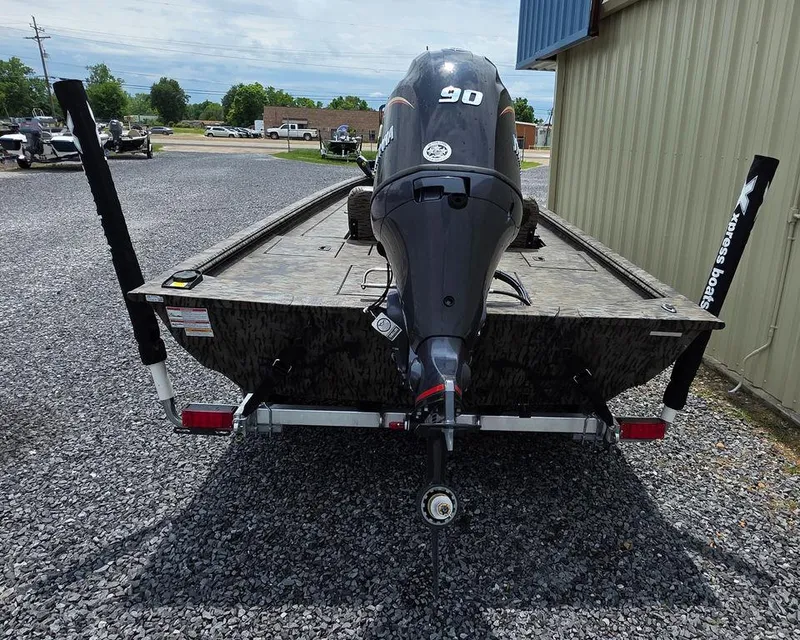 Slide: The Image of 2025 Xpress XP180 boat with outboard motor, parked on gravel near a building. - 22