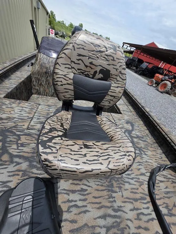 Slide: The Image of 2025 Xpress XP180 boat with camouflage seating, parked near a building and farm equipment. - 9