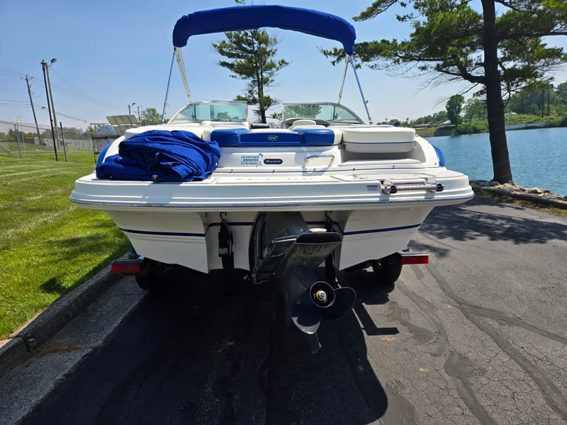 Slide: The Image of 2013 Bryant 210 STE boat with blue canopy, parked near a lake. - 2