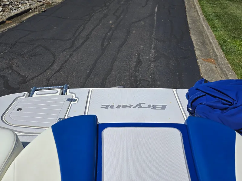 Slide: The Image of 2013 Bryant 210 STE boat on a paved road, featuring blue and white seating. - 24