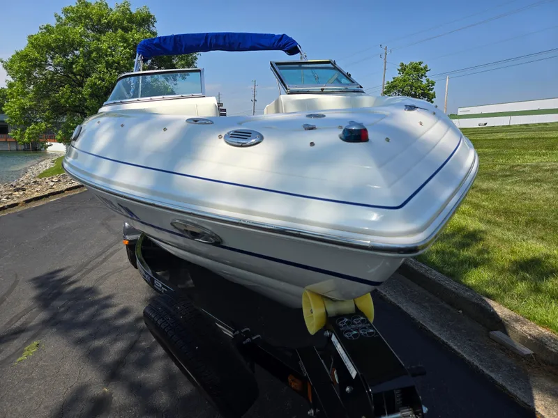 Slide: The Image of 2013 Bryant 210 STE boat on trailer, parked near a lake with trees and grass. - 6