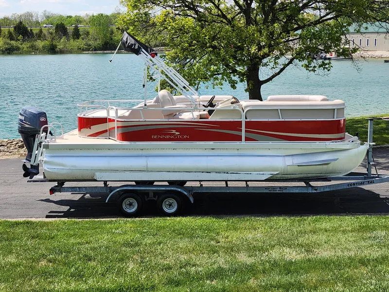 Slide: The Image of 2012 Bennington 22 SSL pontoon boat on trailer by a lake, under a tree. - 0