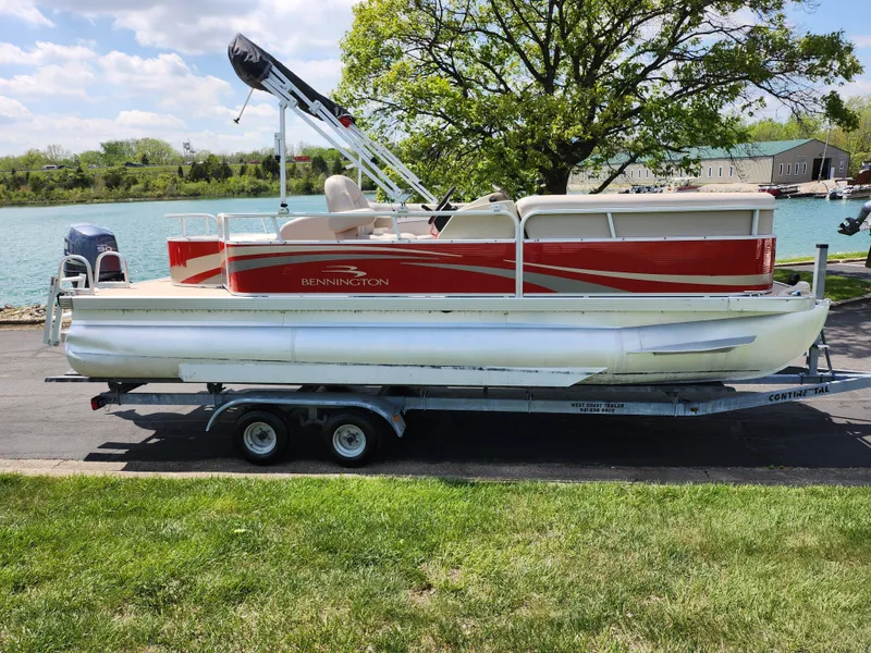 Slide: The Image of 2012 Bennington 22 SSL pontoon boat on trailer by a lake, under a tree. - 10
