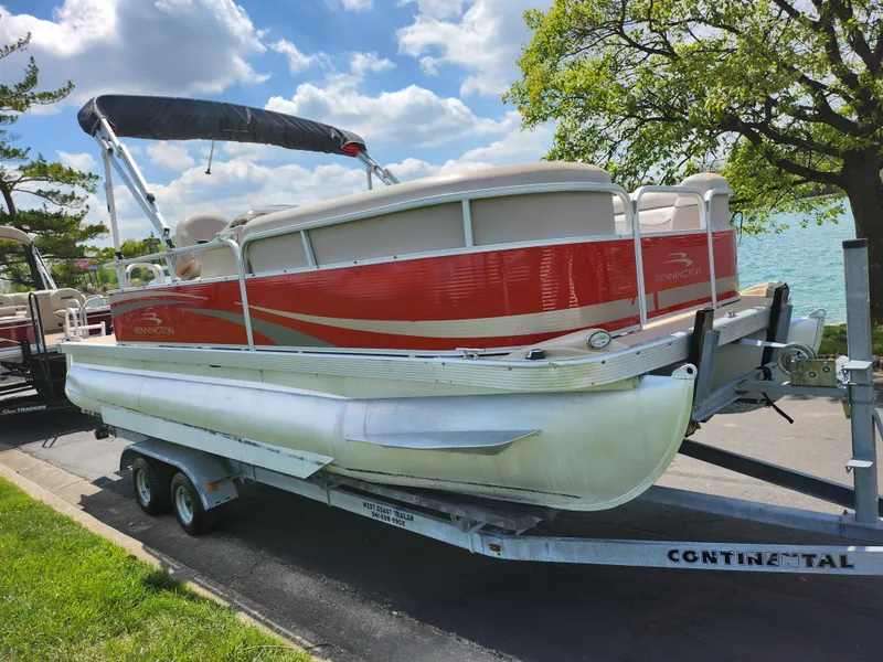 Slide: The Image of 2012 Bennington 22 SSL pontoon boat on trailer, parked by a lake under a blue sky. - 9