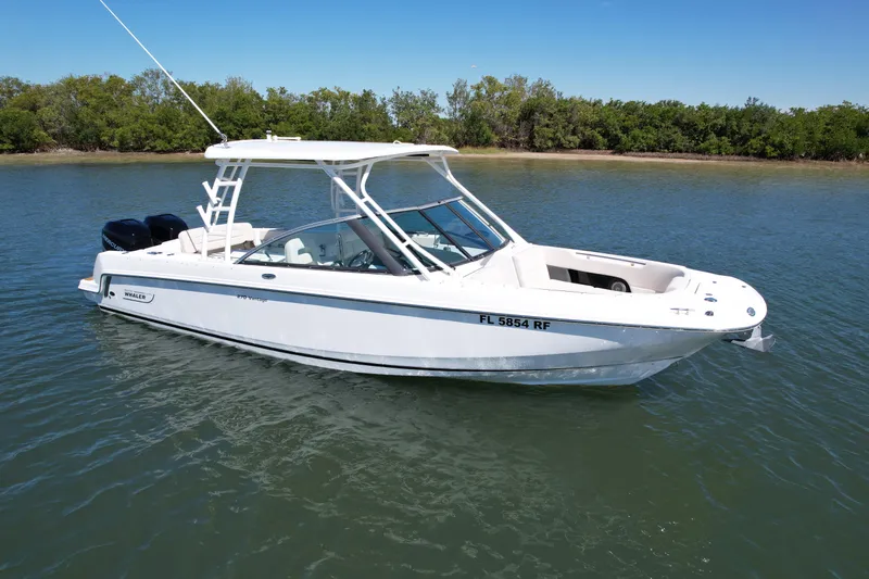 Slide: The Image of 2017 Boston Whaler 270 Vantage boat on calm water, near a tree-lined shore. - 11