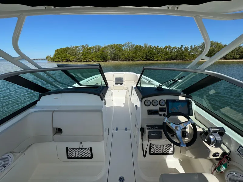 Slide: The Image of 2017 Boston Whaler 270 Vantage boat interior with steering wheel and dashboard, near a scenic shoreline. - 18