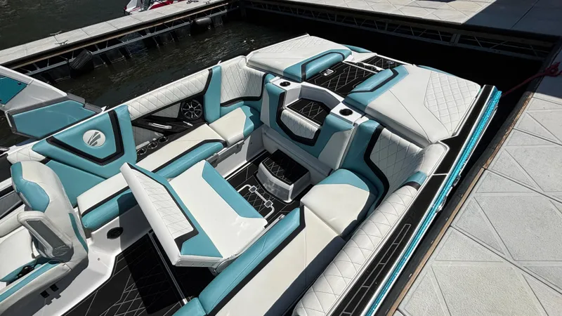 Slide: The Image of 2019 Tigé 25 ZXS boat interior with teal and white seating at a dock. - 15