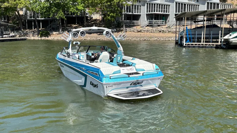 Slide: The Image of 2019 Tigé 25 ZXS boat on a lake near docks and trees. - 6