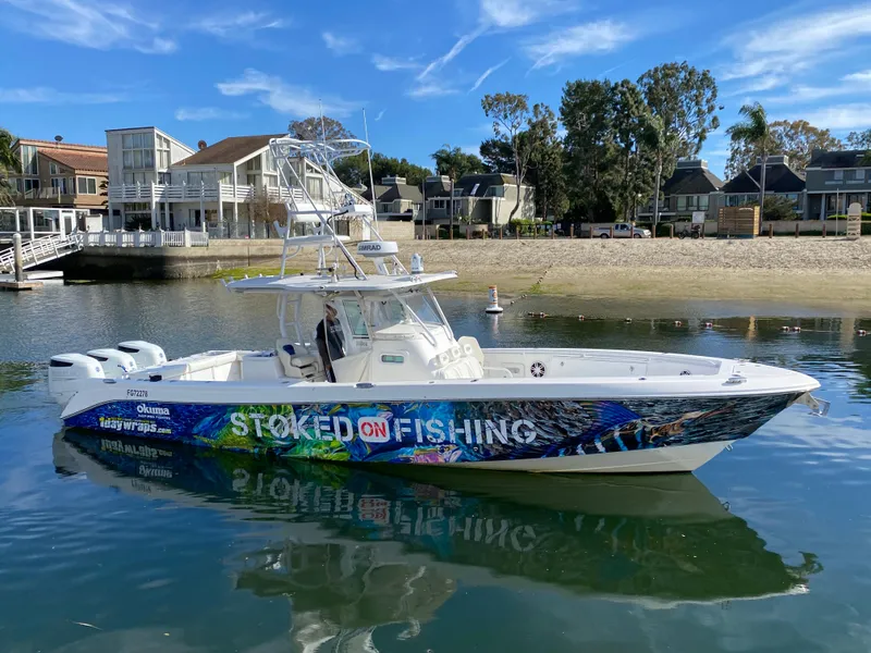 Slide: The Image of 2008 Everglades 355 Center Console boat with vibrant "Stoked on Fishing" design, docked by the shore. - 2