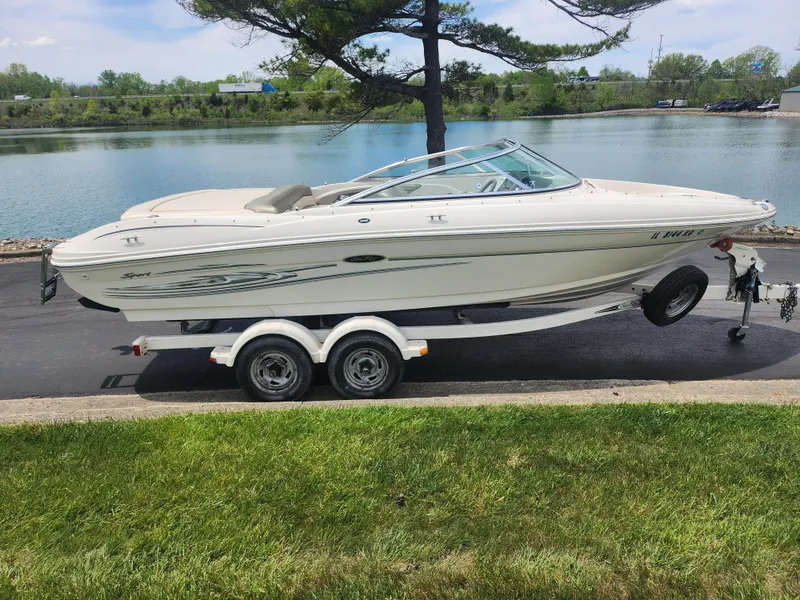 Slide: The Image of 2004 Sea Ray 200 Sport boat on trailer by a lake, surrounded by greenery. - 9