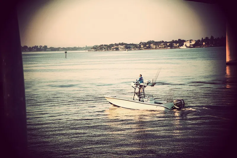 Slide: The Image of 2025 Yellowfin 26 Hybrid boat cruising on calm waters near a coastal town. - 6