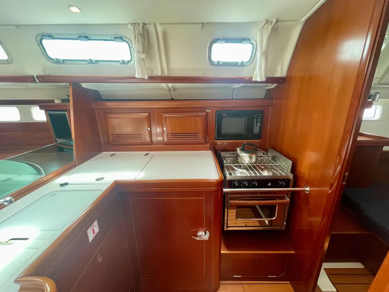 Slide: The Image of 2004 Beneteau Oceanis Clipper 473 yacht kitchen with stove, microwave, and wooden cabinetry. - 19