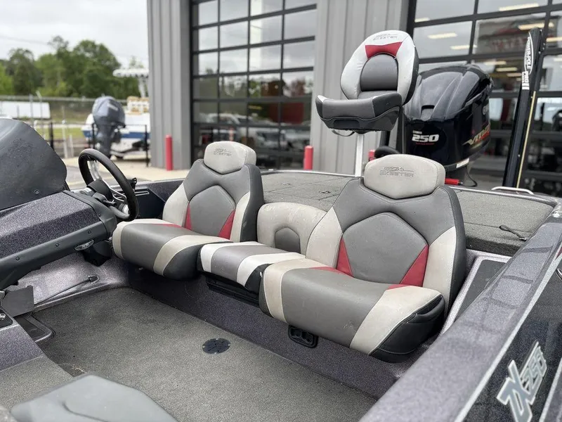 Slide: The Image of 2017 Skeeter ZX250 boat interior with gray and red seating, parked near a garage. - 7