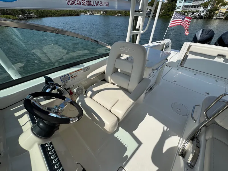 Slide: The Image of 2018 Boston Whaler 270 Vantage boat interior with steering wheel and seating, docked by water. - 20