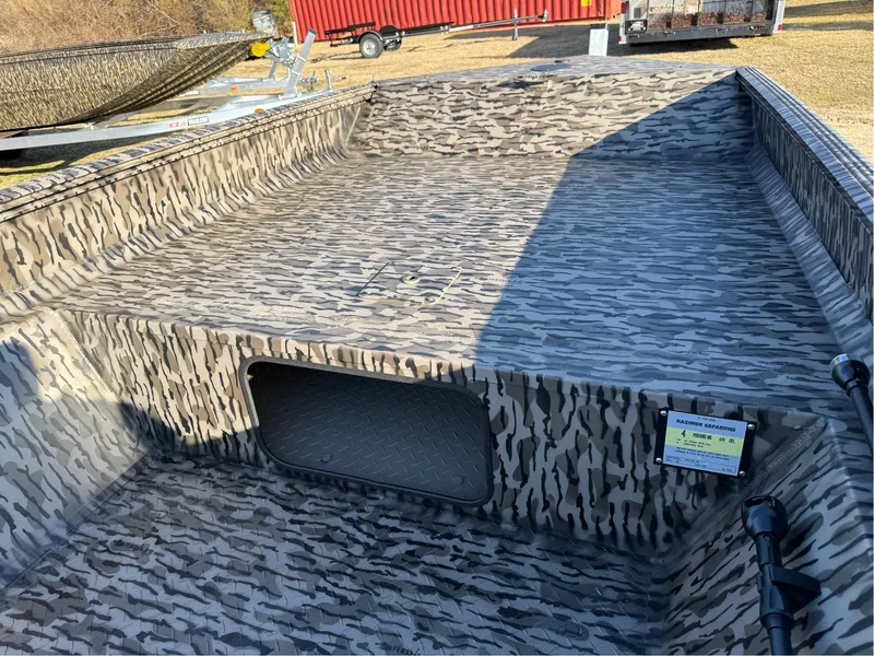 Slide: The Image of 2025 EDGE BOATS 656 SPORTSMAN with camouflage interior, open storage compartment, and trailer in background. - 6