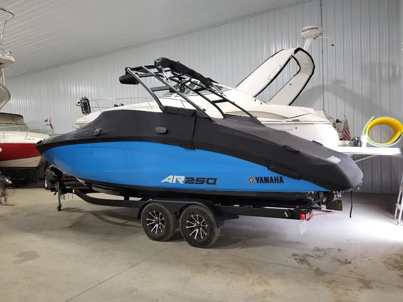 Slide: The Image of 2023 Yamaha AR250 boat in storage, blue hull, covered, on trailer. - 16