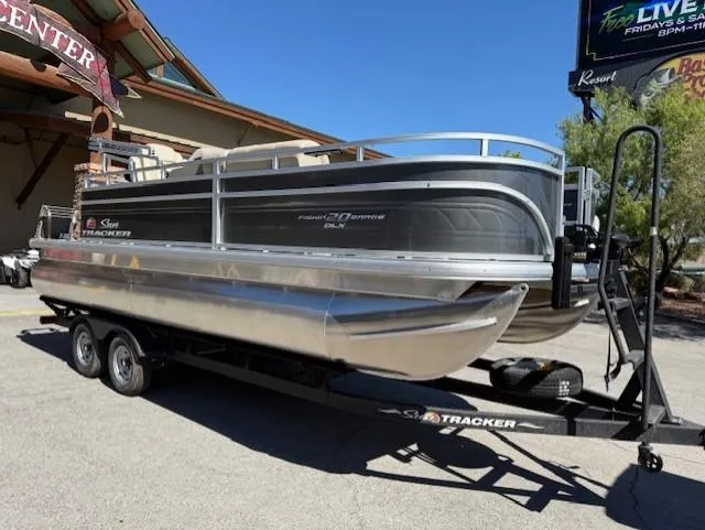 Slide: The Image of 2025 Sun Tracker Fishin' Barge 20 DLX pontoon boat on trailer, parked outdoors. - 2