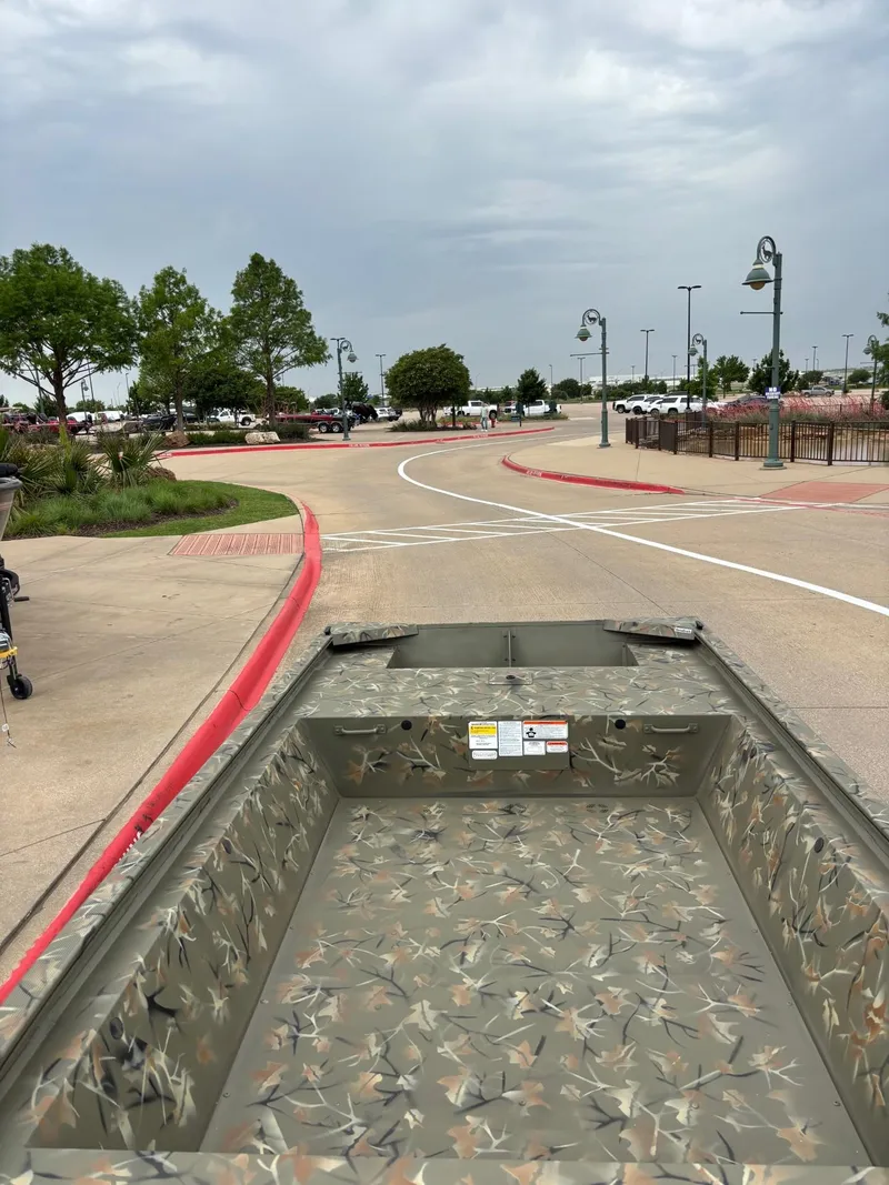 Slide: The Image of 2025 Tracker Grizzly 1648 Jon boat on a paved road with trees and cloudy sky. - 5