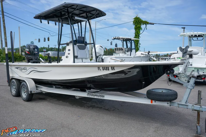 Slide: The Image of 2016 Blue Wave 2200 STL boat on trailer, parked outdoors, with T-top and dual-axle trailer. - 14