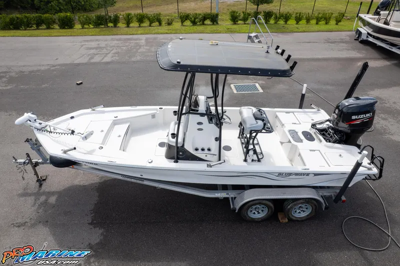 Slide: The Image of 2016 Blue Wave 2200 STL boat on trailer with Suzuki outboard motor, parked outdoors. - 3