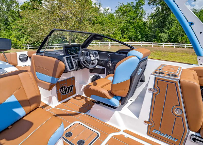 Slide: The Image of 2024 Malibu Wakesetter 24 MXZ interior with brown and blue seating, modern dashboard, and lush greenery backdrop. - 21